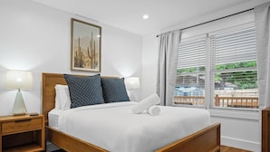 A neatly made bed with white and patterned pillows, a wooden headboard, and a nightstand with a lamp. - Freshly Renovated 2BR in E Austin High End Finishes Near Downtown Nightlife (Austin)
