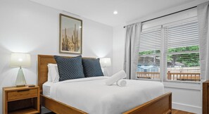 Una cama bien hecha con almohadas blancas y estampadas, un cabecero de madera y una mesita de noche con una lámpara.