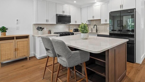 A modern kitchen with white cabinets, a central island with bar stools, a microwave, and a refrigerator. - Freshly Renovated 2BR in E Austin High End Finishes Near Downtown Nightlife (Austin)