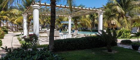 A pool area with a pergola, palm trees, and lounge chairs.