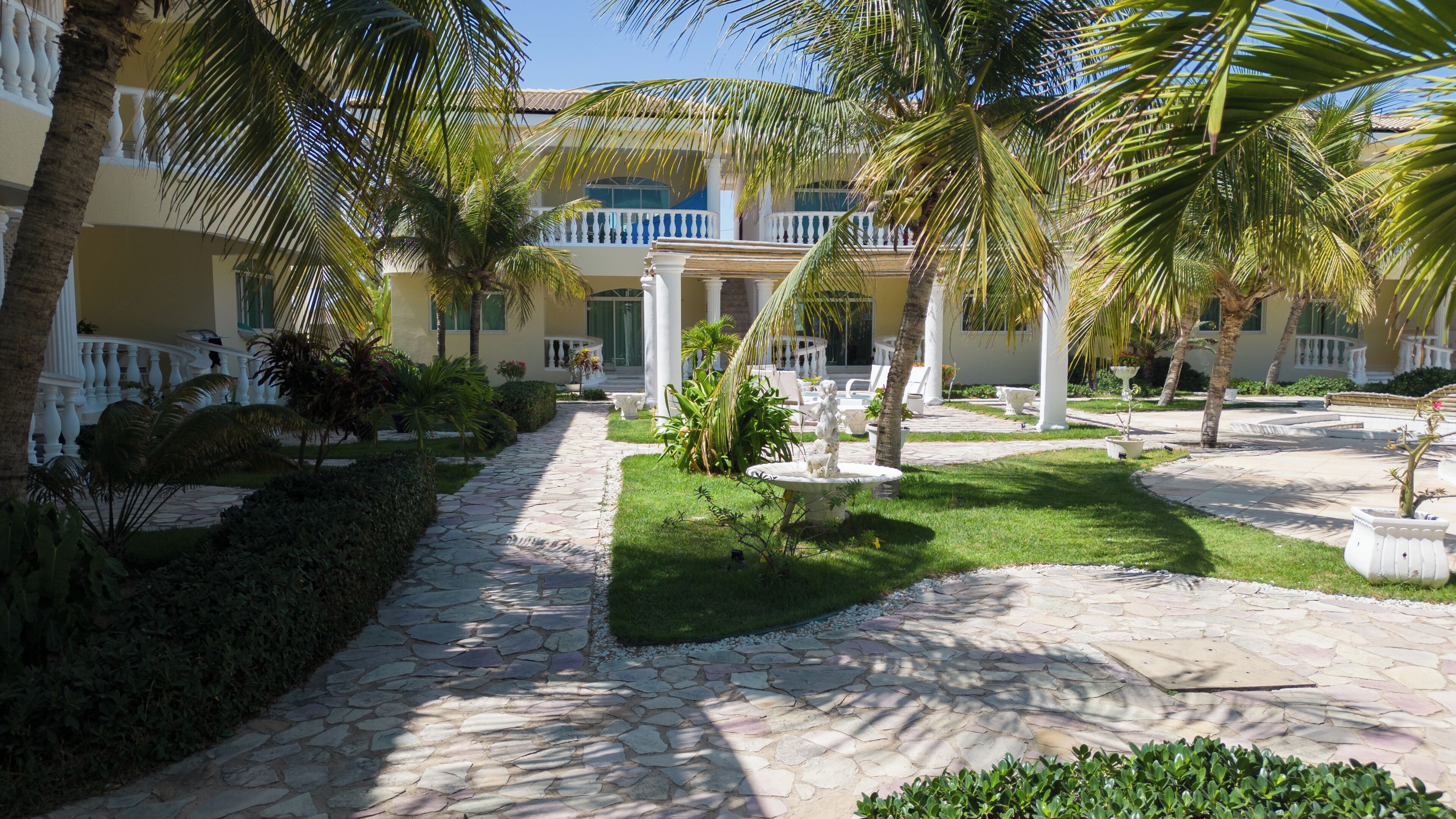 A courtyard with a stone pathway, palm trees, and a building with balconies.