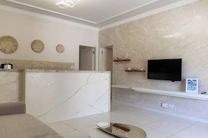 A lobby with a reception desk, a flat-screen TV, marble walls, and a tiled floor. - Green Paradise Residence (Aracati)