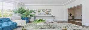 Ein Wohnzimmer mit einem blauen Sofa, einem Couchtisch mit Pflanzen, einem Bild an der Wand und einer Tür zu einem anderen Raum.