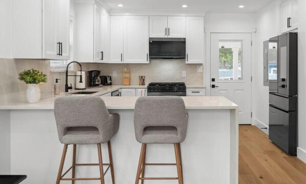 Une cuisine moderne avec des meubles blancs, une cuisinière noire et deux tabourets de bar gris.