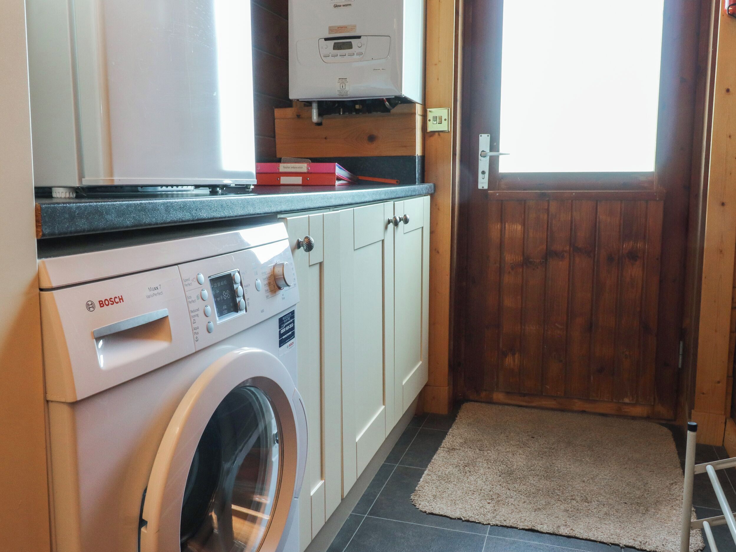 A compact kitchen with a Bosch washing machine, a built-in oven, and a wooden door.