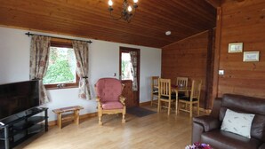 A wooden interior with a TV, a pink armchair, a dining table with chairs, a brown sofa, and a chandelier. - Chestnut Lodge (Preston)