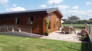 A wooden cabin with a patio, a small garden, and a metal fence. - Chestnut Lodge (Preston)