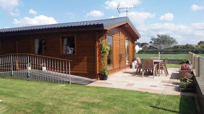 Eine Holzhütte mit Terrasse, kleinem Garten und einem Metallzaun.