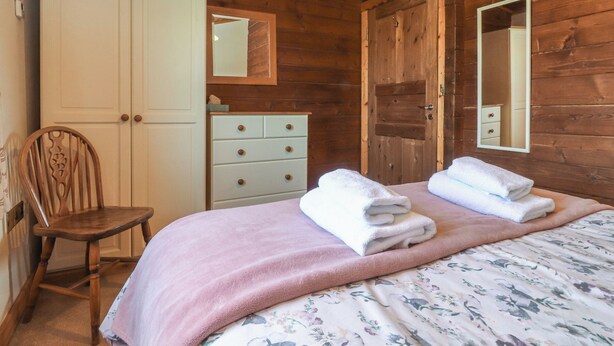 A wooden room with a bed, a chair, a dresser, and a mirror. - Chestnut Lodge (Preston)