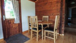 A wooden interior with a door, a window with curtains, a round table with chairs, and a doormat. - Chestnut Lodge (Preston)