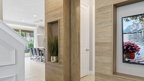 Un pasillo con una puerta de madera, un cuadro enmarco de un paisaje y una planta en maceta.