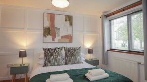 A neatly arranged bedroom with a bed, two bedside lamps, a hanging light fixture, a window with blinds, and a wall-mounted abstract painting. - 39 Knocknagael (Inverness)