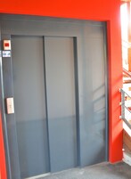 Puerta cerrada de ascensor con panel de control a la izquierda, sobre un fondo rojo.