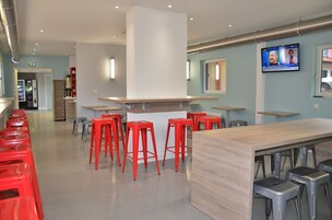 Zona de bar moderna con taburetes rojos, una barra de madera y una pantalla de televisión mostrando un noticiero.