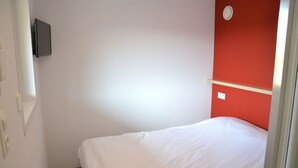 A room with a bed, a red accent wall, a mounted TV, and a light switch. - Eklo Hotels Le Mans (Le Mans)