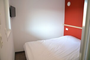 Una habitación con cama, pared de acento roja, televisor montado y un interruptor de luz.
