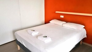 A single bed with white linens, two towels, and a bedside table with a lamp.