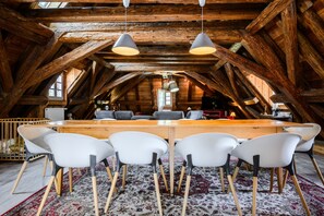 Um quarto no sótão com teto de madeira, uma mesa de jantar com cadeiras e luminárias pendentes.
