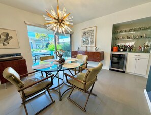 Et moderne spiseområde med et glasbord, polstrede stole, en usædvanlig lysekrone og et køkken med glashylder.