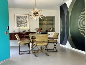 Ein moderner Essbereich mit einer Kronleuchter, einem gerahmten Kunstwerk und einer Bar mit Regalen.