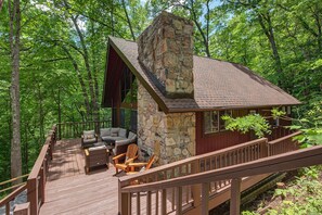 Eine Holzhütte mit Steinkamin, einer Holzterrasse und einer Sitzgelegenheit im Freien, umgeben von Bäumen.