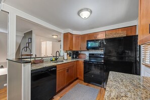 Eine Küche mit Holzschränken, einem schwarzen Kühlschrank, einer Mikrowelle und einem Geschirrspüler.