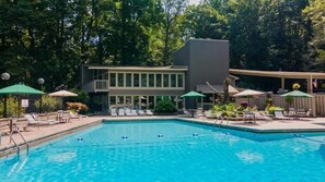 Ein Swimmingpool mit Liegestühlen und Sonnenschirmen, umgeben von Bäumen und einem Gebäude mit einem Balkon.