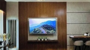 Quarto de hotel com duas camas, televisão fixada na parede, escrivaninha e luminária moderna.