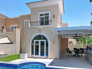 Ein zweistöckiges Haus mit Terrasse, Sitzgelegenheiten im Freien und einem Swimmingpool.