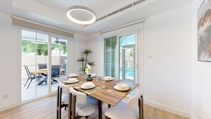 Un espace repas moderne avec une table en bois dressée pour quatre personnes, de grandes fenêtres et une vue sur l’extérieur.
