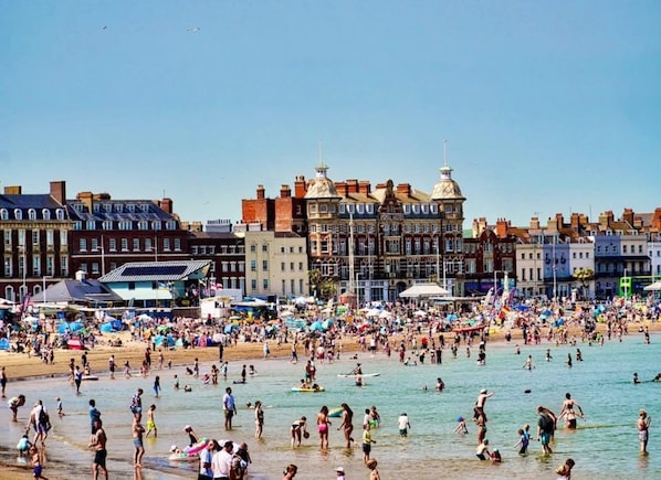 A beachside hotel with a prominent Royal Hotel sign, a sandy beach, and a clear blue sky.