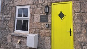 A stone building with a yellow door, a window, and a sign that reads 'Boatswain's Watch.' - Boatswains Watch, Sleeps 4, Pet Friendly (Portland)