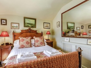 A hotel room with a large bed, two bedside tables, a mirror, and framed pictures on the walls.