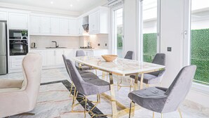 Una cocina moderna con armarios blancos, encimera de mármol y un comedor con mesa de mármol y sillas tapizadas en gris.