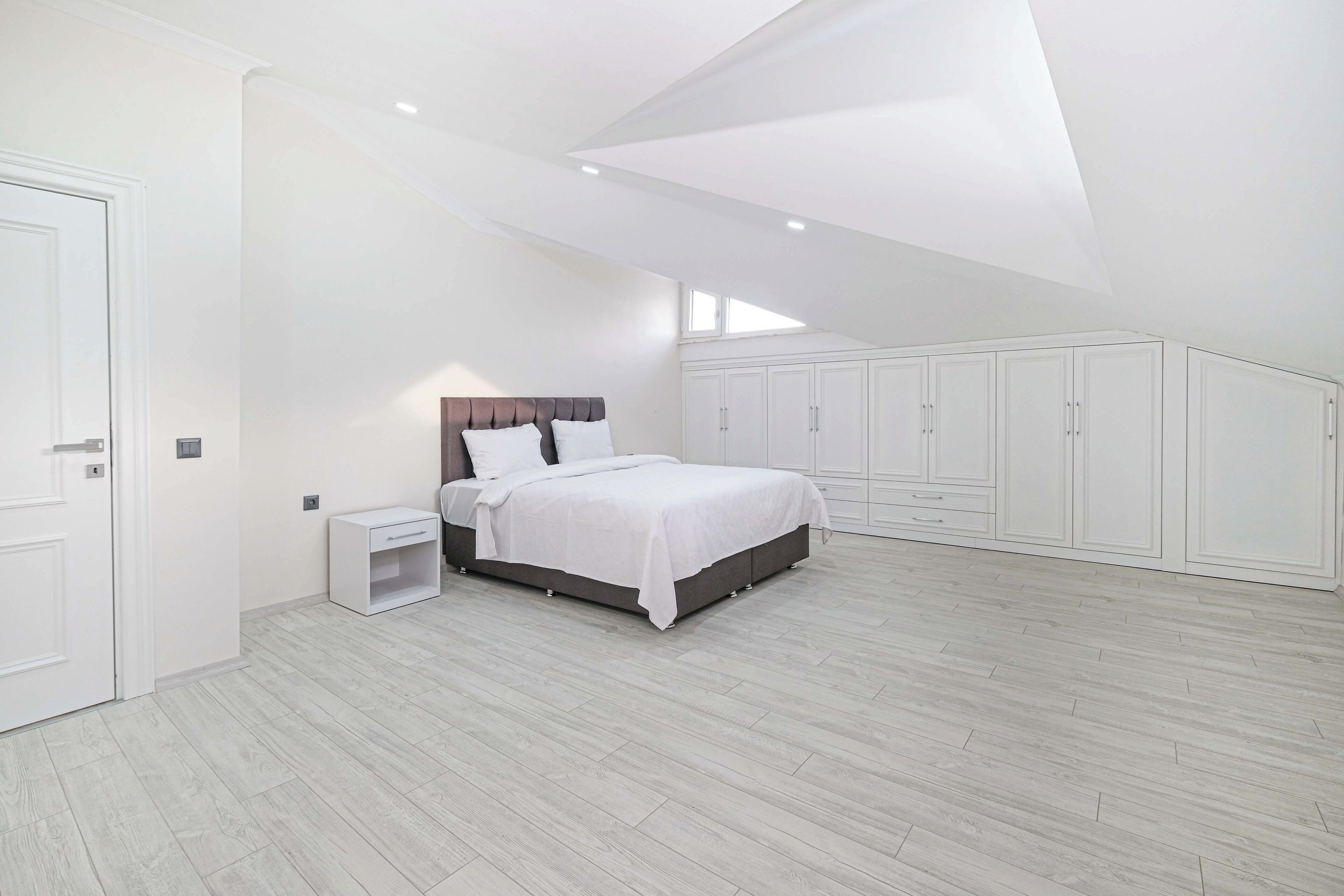 A bedroom with a bed, nightstands, a wardrobe, and a sloped ceiling.
