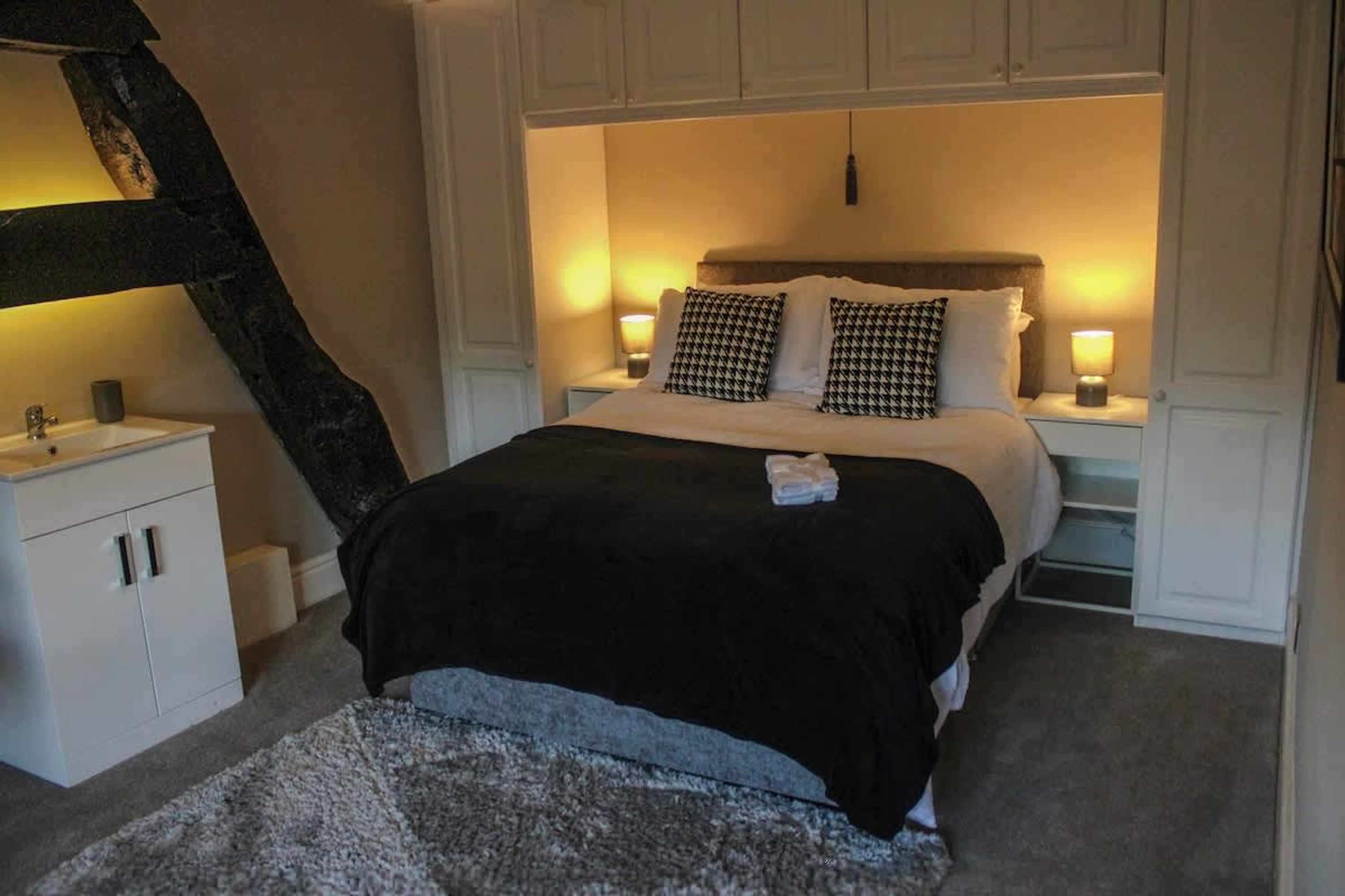 A bedroom with a bed, bedside tables, a nightstand, a lamp, and a carpeted floor.