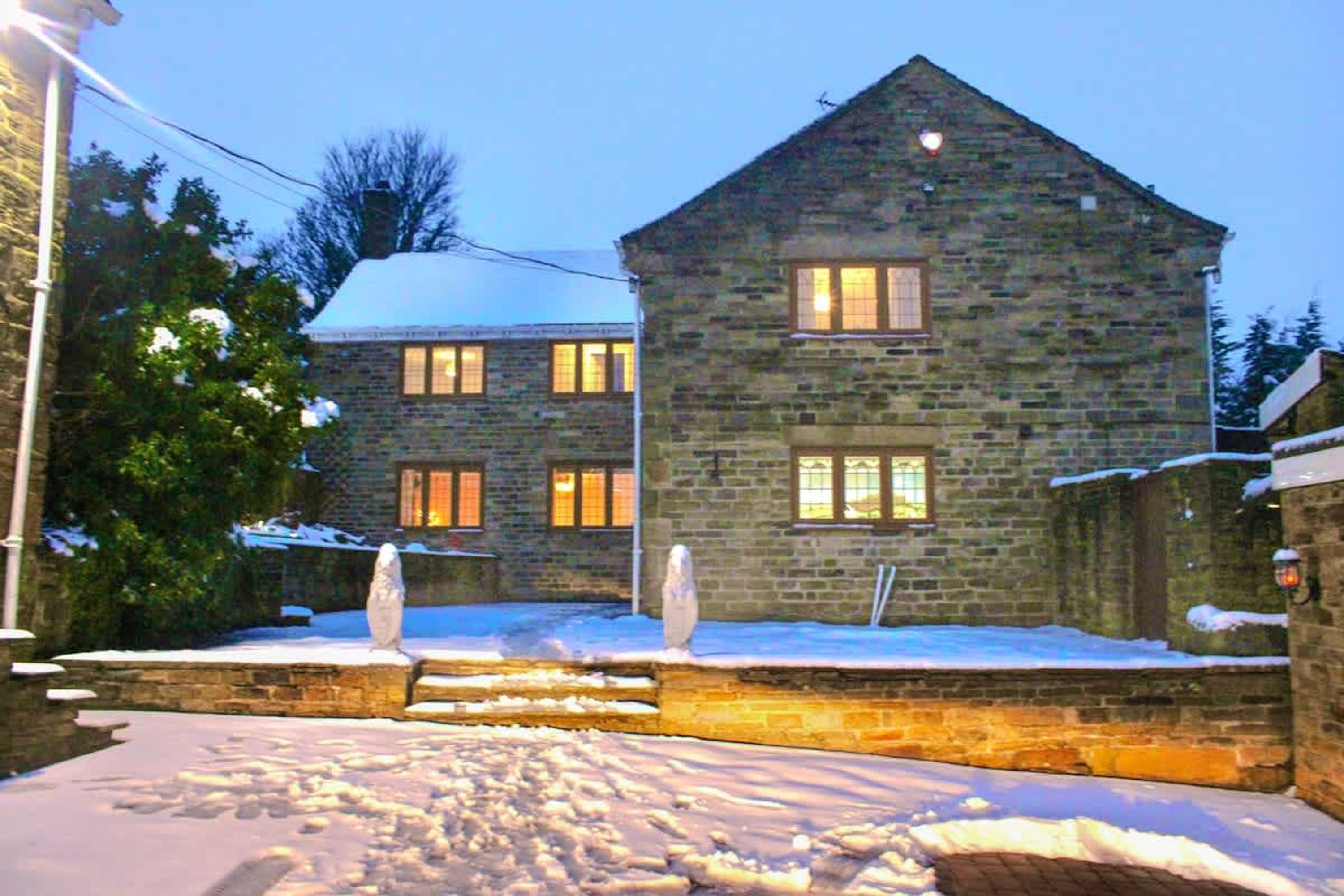 A stone building with multiple windows, a snow-covered ground, and a brick pathway leading to the entrance.