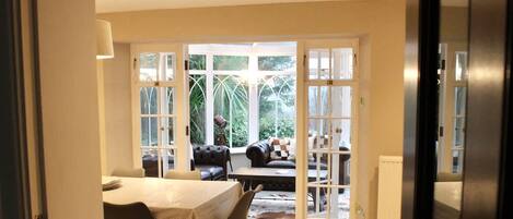 An open-plan living area with a dining table, sofas, and a view through large glass doors.