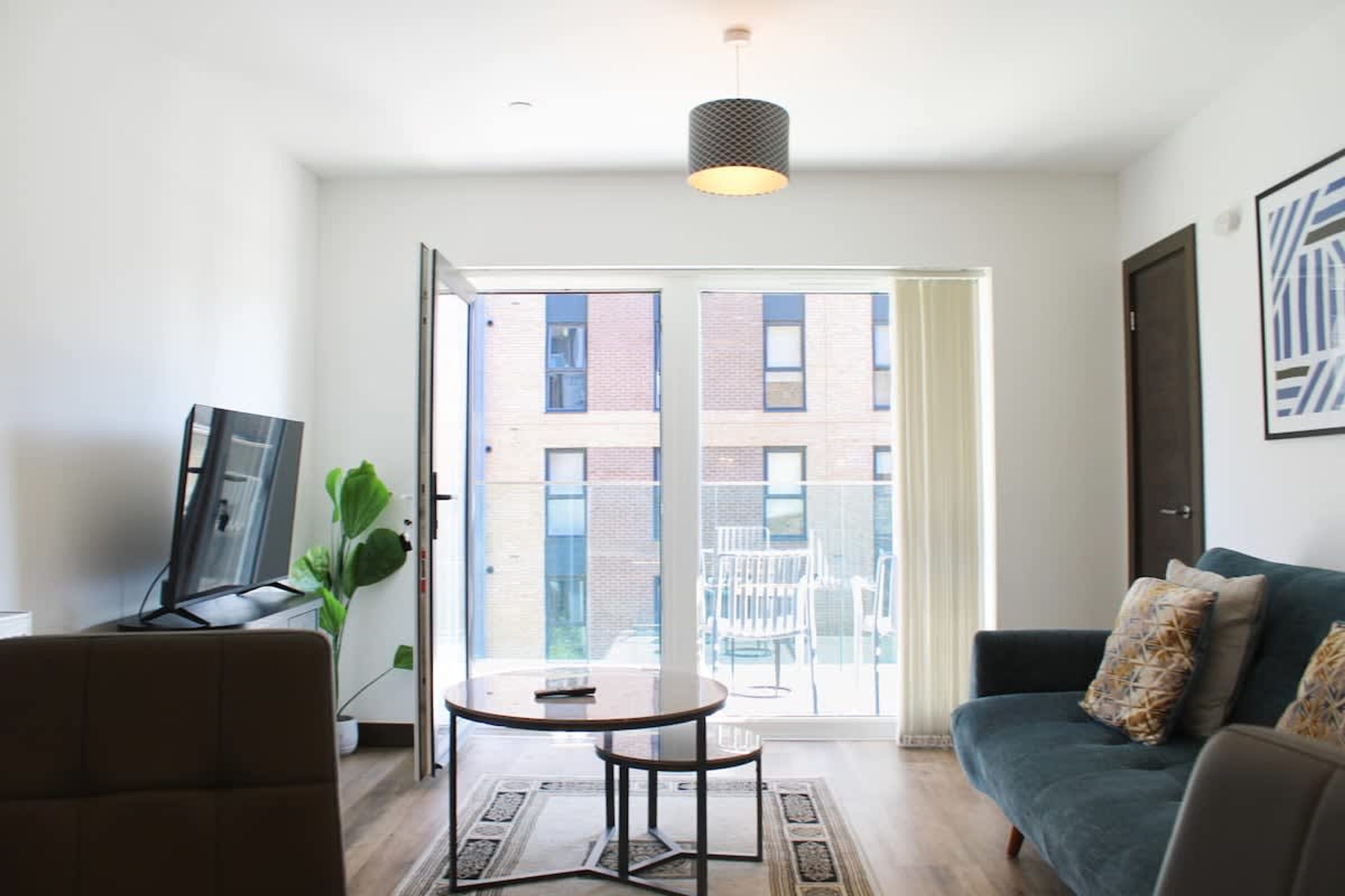 A modern living room with a sofa, a small round table, a TV, and a large window with a view of buildings.