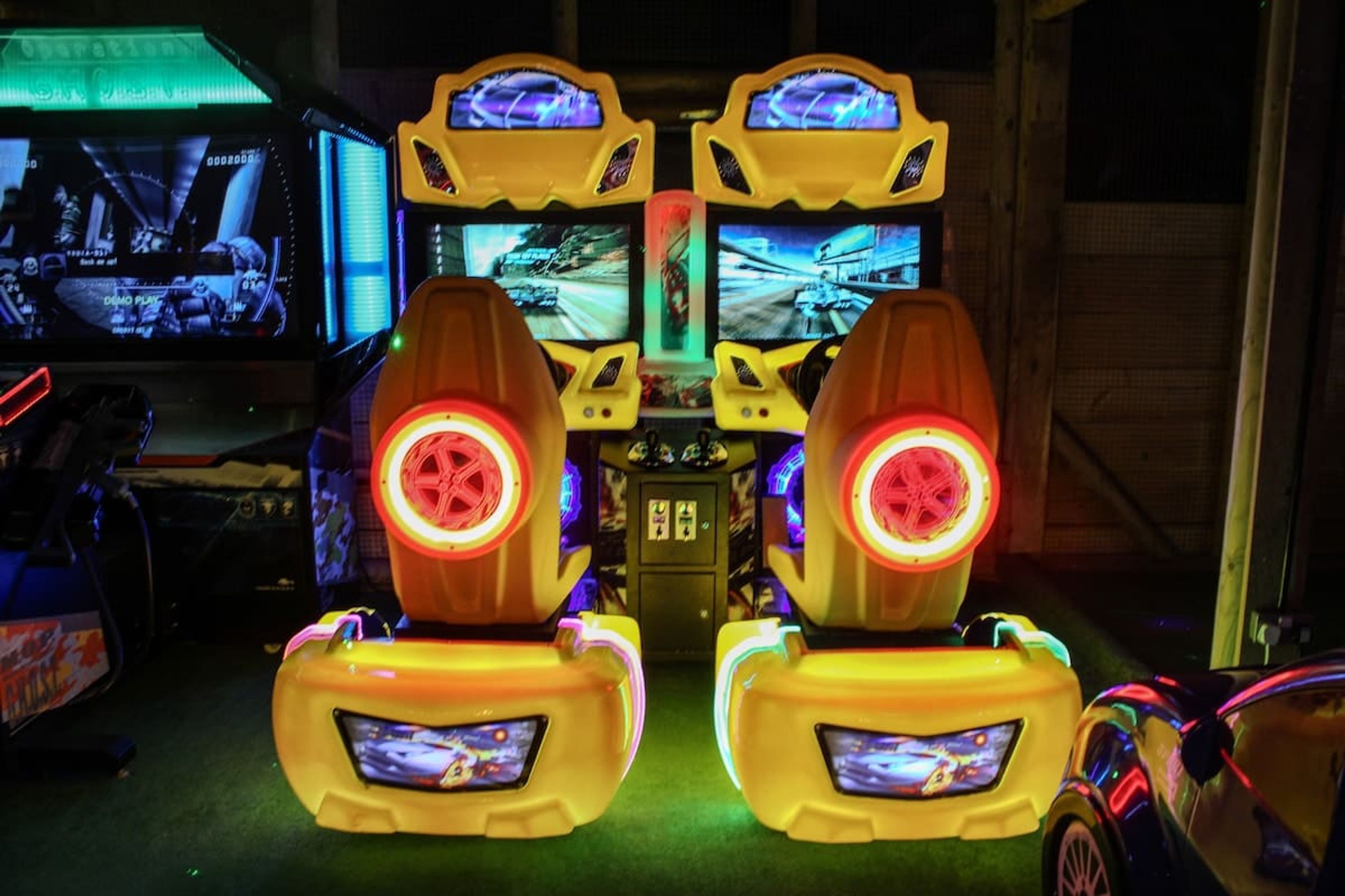 Twee spelautomaten voor racegames met schermen en verlichte zitplaatsen.