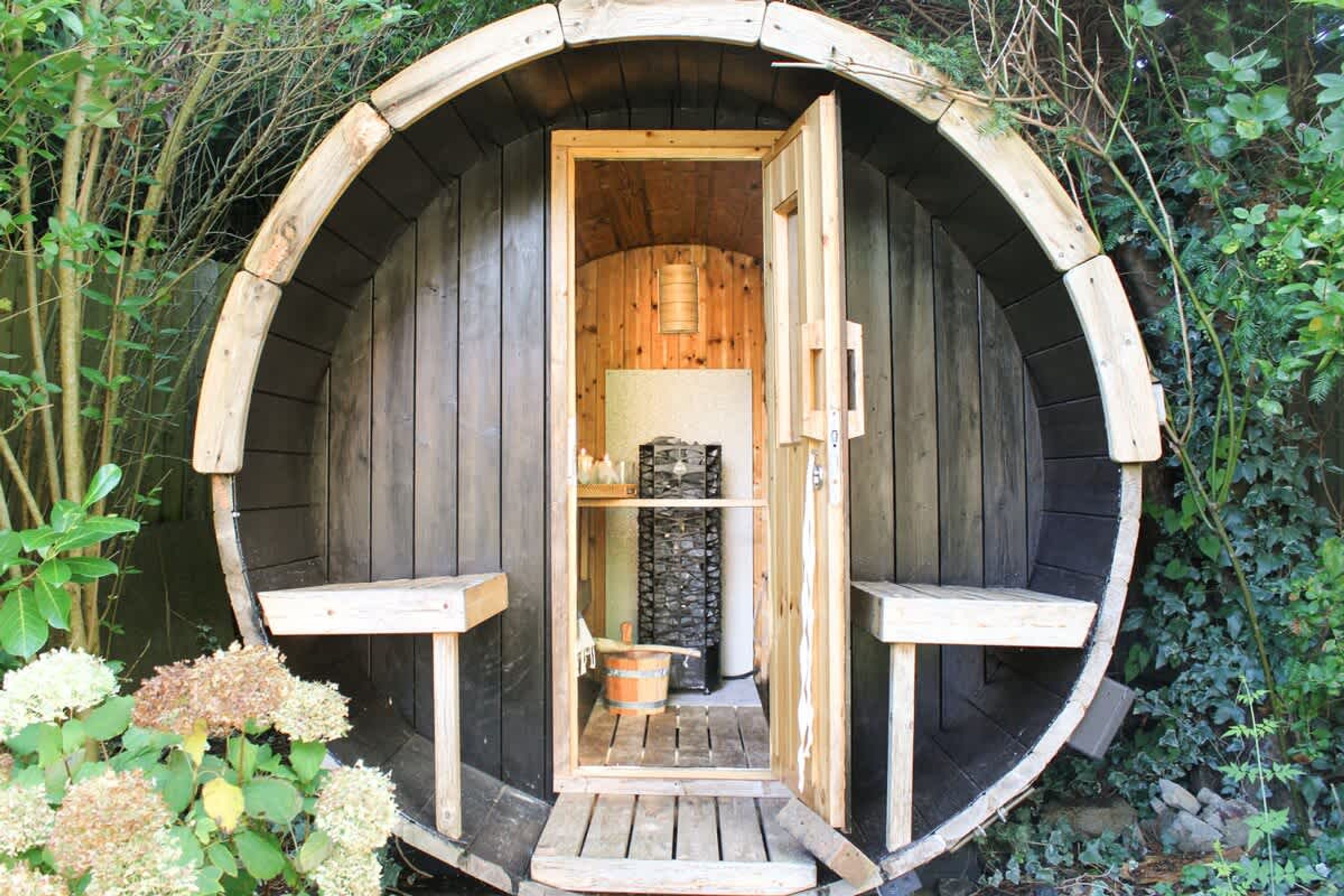 A wooden sauna with a circular design, a bench, and a small table inside.