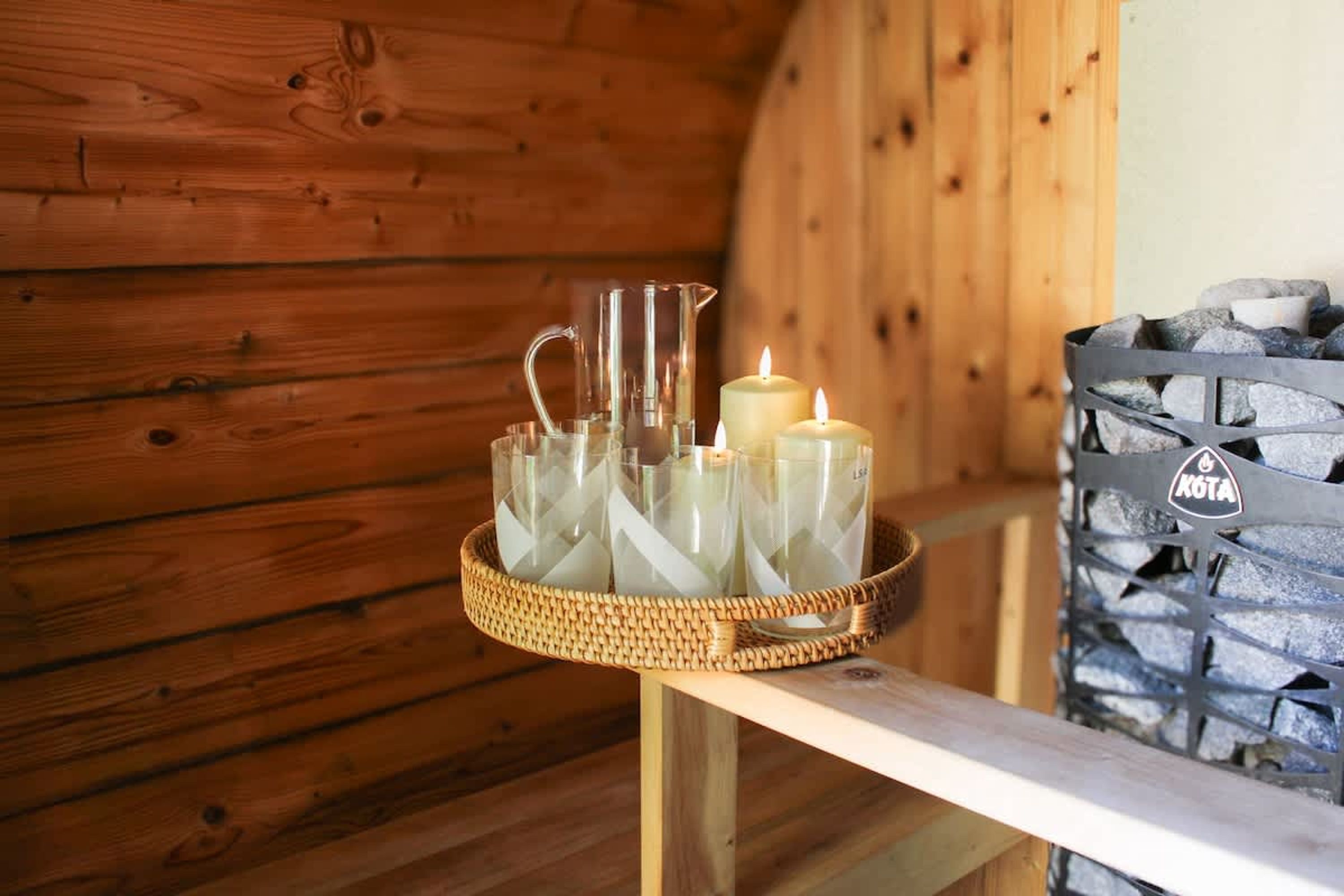 Een houten interieur met een rieten dienblad waarop kaarsen en een glazen kruik staan.