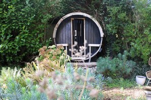 A rustic wooden structure with a door, surrounded by lush greenery and plants. - Lewes Sauna House Characterful Interiors Castle Views (Lewes)