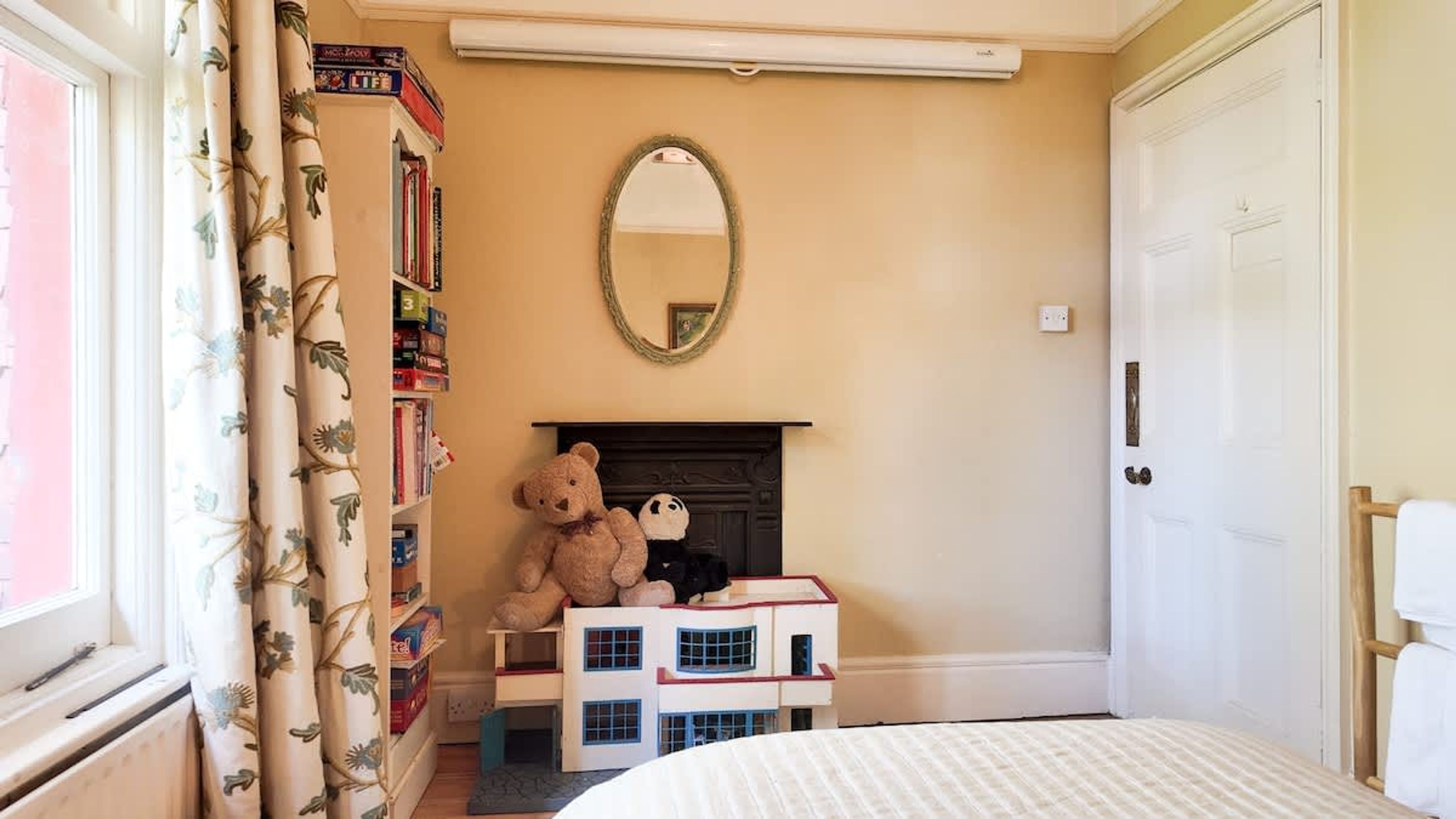 A child's room with a bookshelf, a teddy bear, a mirror, and a fireplace.