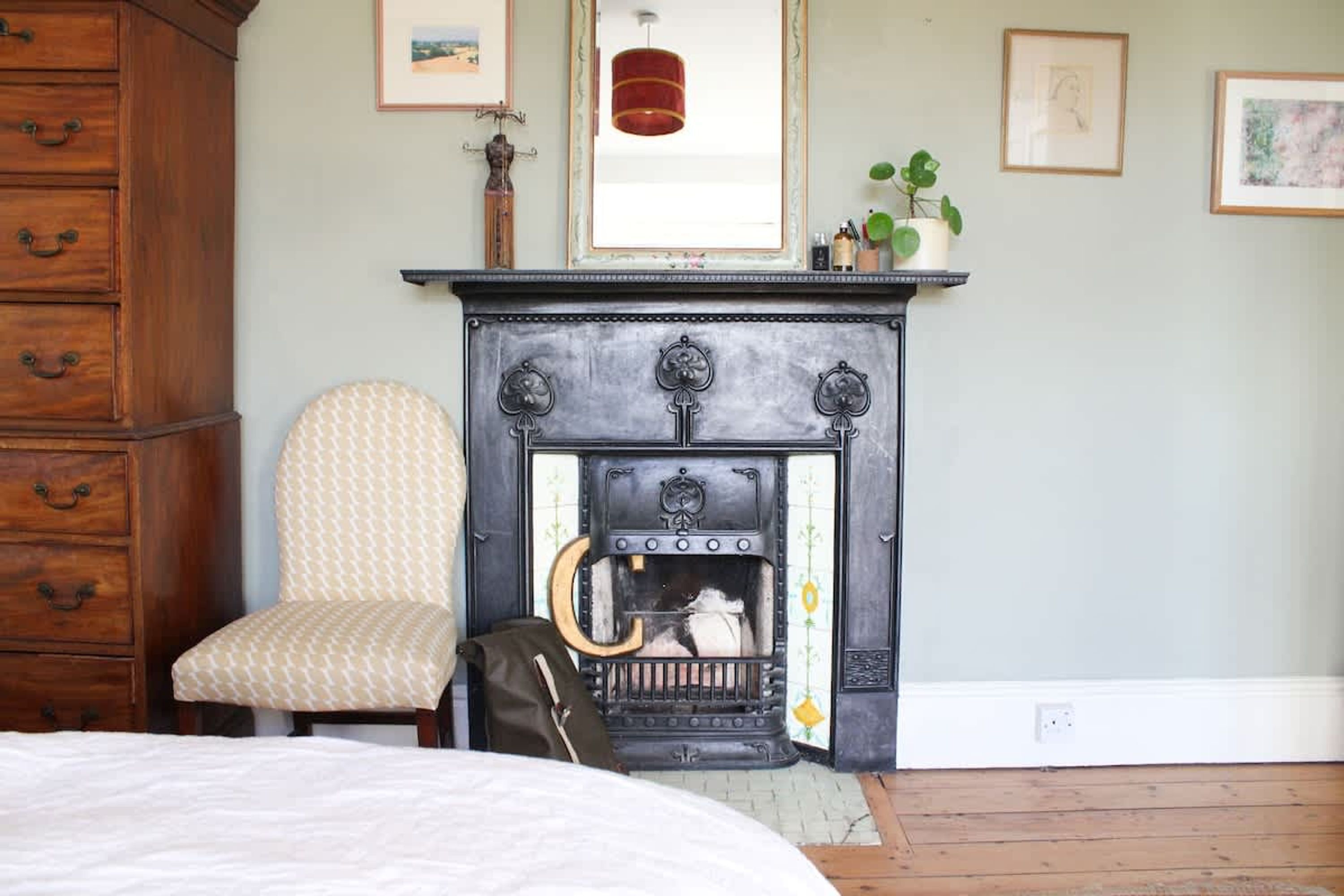 A bedroom with a wooden dresser, a patterned armchair, a fireplace, and a bed.