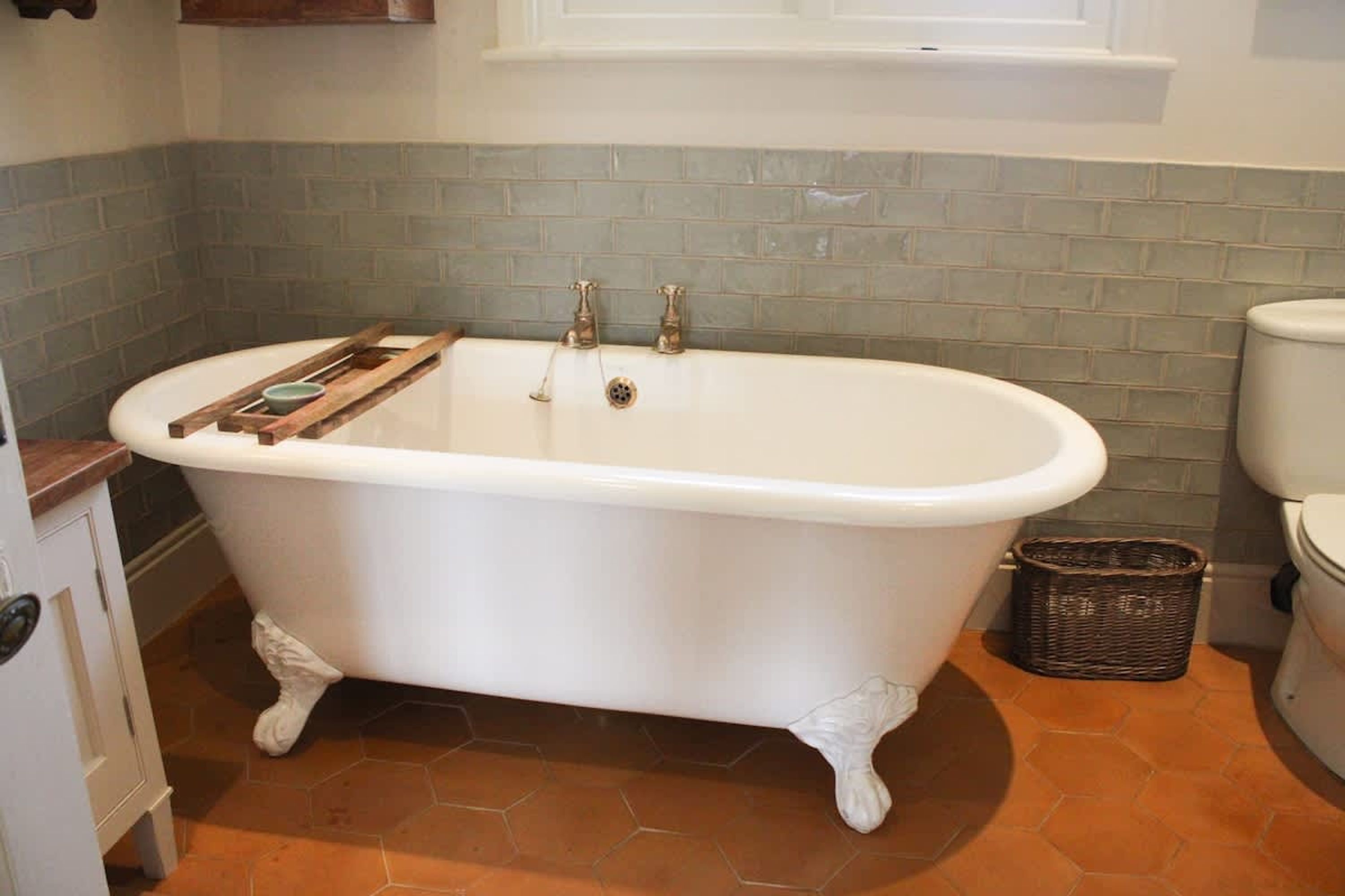 A bathroom with a clawfoot bathtub, a white toilet, and a wicker basket on the floor.