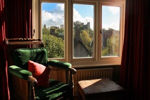 A room with a view of a castle, a wicker chair with a green cushion, and a wooden table. - Lewes Sauna House Characterful Interiors Castle Views (Lewes)