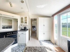 A compact kitchen with white cabinetry, a stove, and a dining area with a patterned rug. - Berney Lodge - Puppy Lounge Arcades Games Room (Market Rasen)