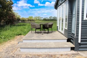 A small house with a porch, two wicker chairs, and a table. - Berney Lodge - Puppy Lounge Arcades Games Room (Market Rasen)