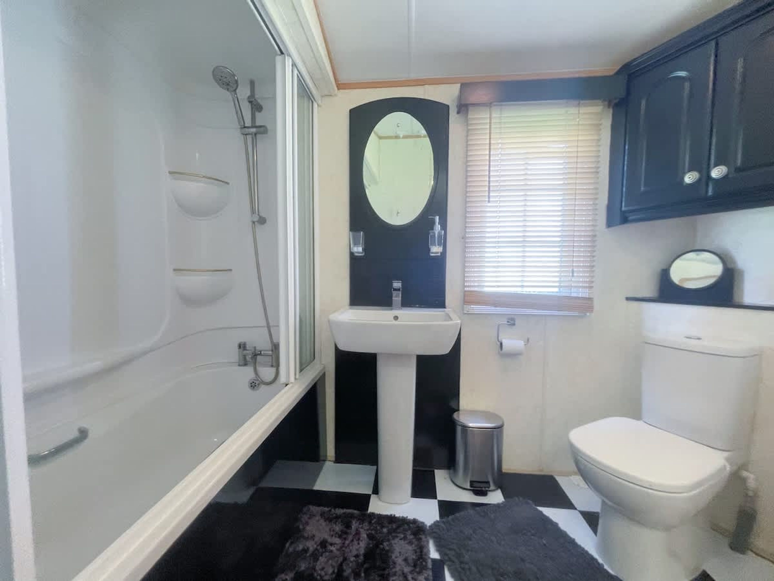 A compact bathroom with a bathtub, a pedestal sink, a toilet, and a mirror.